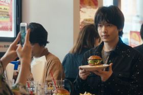 ハンバーガー撮影の目的は？手前に見える手の主は？