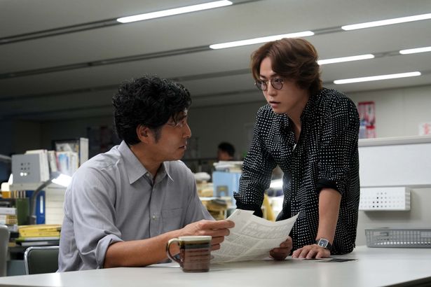 編集長の堂前にでき上がった原稿を見せる鳴海