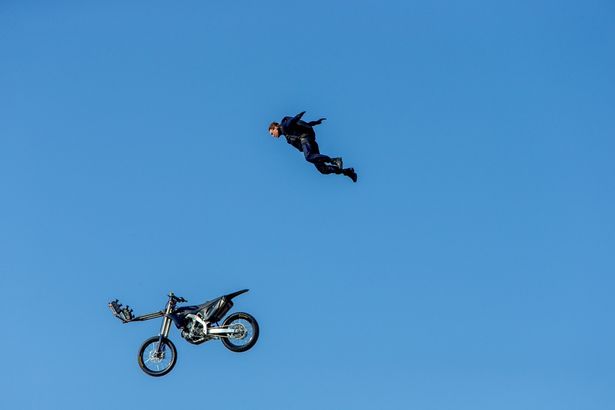 【写真を見る】山々に囲まれた断崖絶壁からバイクごと空中にダイブするド迫力の超絶スタント！