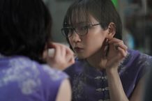 紫のチャイナ服をまとい、鏡越しにピアスを見つめる令子