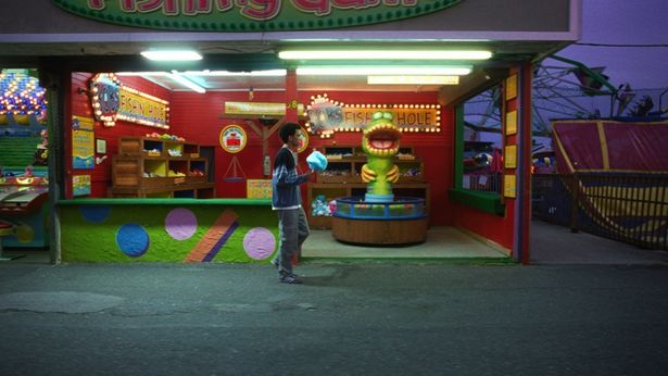 どこかへ行きたいのにどこへも行けない葛藤を抱えながら小さな遊園地で綿菓子を持ち退屈そうに歩くオーウェン