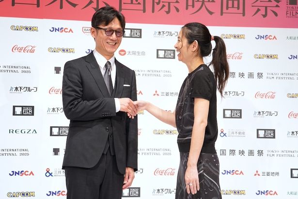 カメラマンのリクエストに応え照れながら握手をする二人