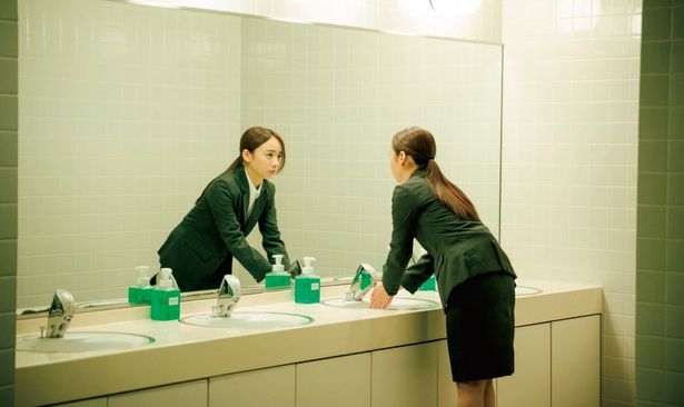 スーツ姿で不安を抱えながら鏡越しに自分と対峙する様子