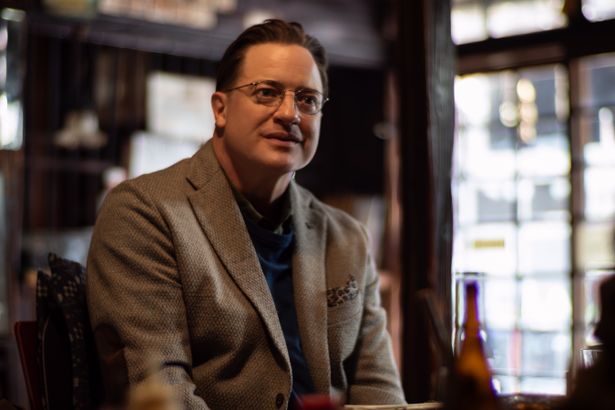 眼鏡とツイードジャケットを身に付けて穏やかな表情を浮かべる姿