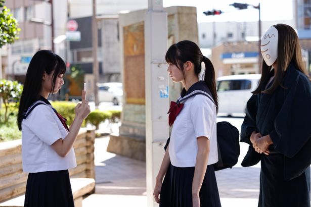 まいきち演じる皐月が撮影する美咲の後ろには、和服＆お面姿の神様が
