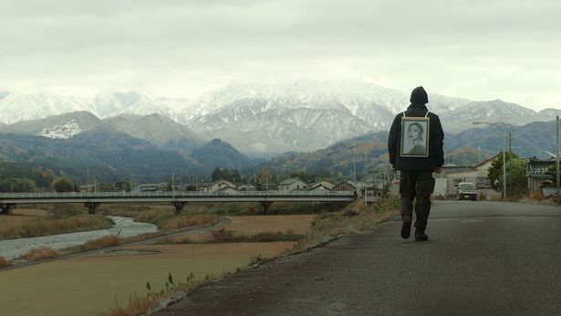 果てしなく続く山景色のなか、妻の遺影を手にさまよう信治