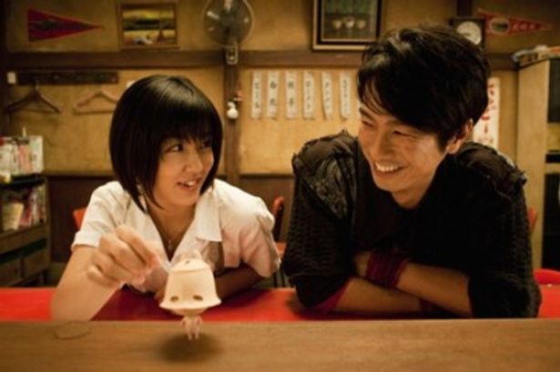 【写真】カノン(里久鳴祐果)とタイヘイ(眞島秀和)。テーブルにいるのは埴輪が転生したオンバケ“ブチンコ”