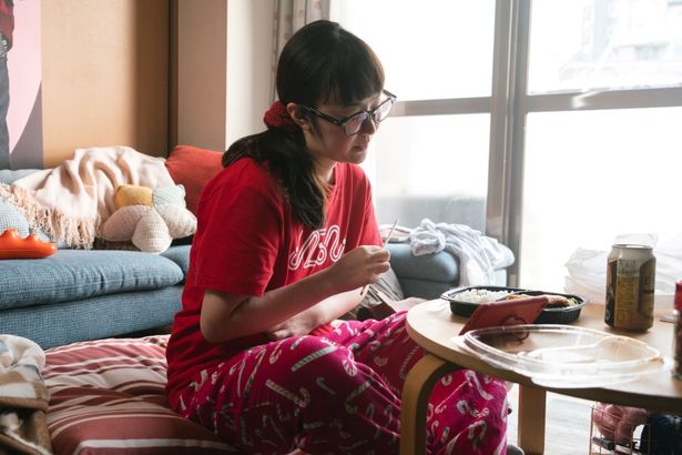 ラフな部屋着姿でコンビニ弁当を頬張りながらスマホで推しの動画を見つめる姿