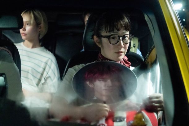 清恵(黒木)が推し活のうちわを手にシンガポールの街をタクシーで麻由と移動するカット