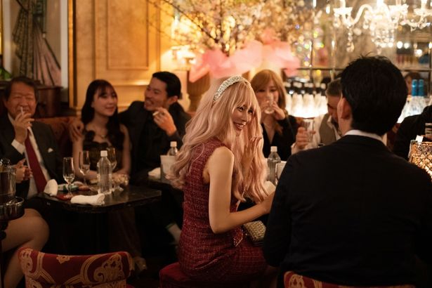 ネオンきらめく店内でキャバ嬢として完璧な笑顔で接客する麻由