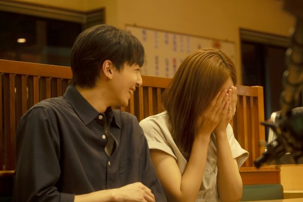 【写真を見る】飲食店で取材を受けながら顔を覆って照れ笑いをする和とそれを見守る将一