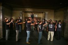輪になって銃を構える男たち。だが、その服装はちょっと変だ