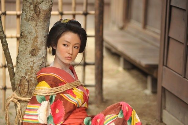 【写真を見る】木に縛りつけられてしまったお咲。鋭い目つきが印象的
